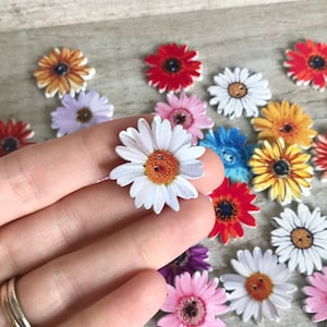 May include: Assortment of colorful wooden flower buttons with two-hole centers. The buttons feature various flower designs, including daisies, sunflowers, and gerberas.