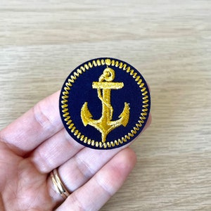 Könnte beinhalten: Ein runder, marineblauer Patch mit einem goldenen gestickten Anker und einem goldenen gestickten Rand.