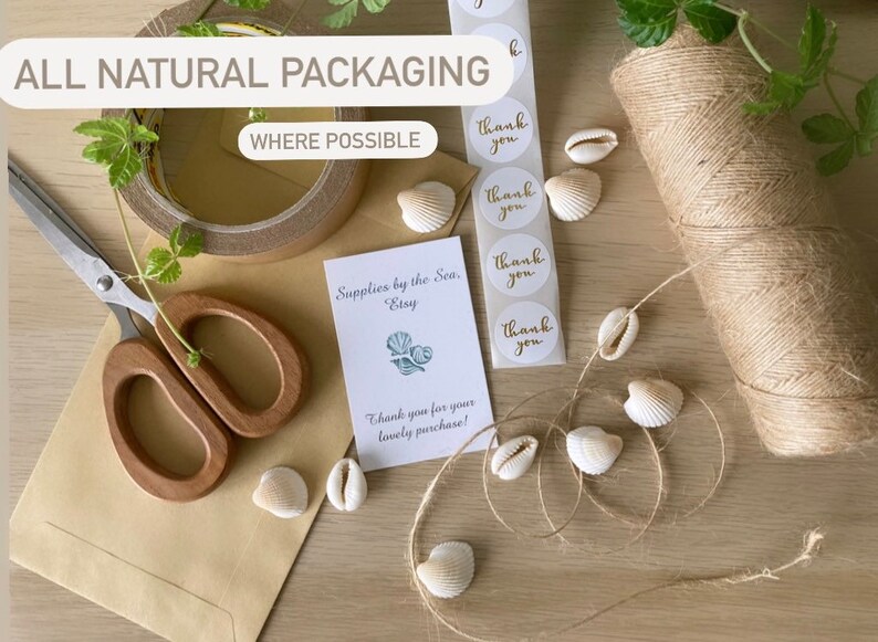 May include: A close-up of a brown paper envelope with a pair of wooden handled scissors, a roll of brown twine, and a small card that reads "Supplies by the Sea, Etsy" and "Thank you for your lovely purchase!"  The card is decorated with a small illustration of seashells.  There are also several small white seashells and a sheet of round stickers that say "Thank you" in gold lettering.