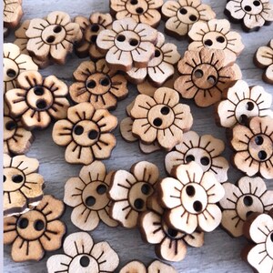 May include: A collection of wooden flower-shaped buttons with two holes each. The buttons are light brown and have a natural wood grain.