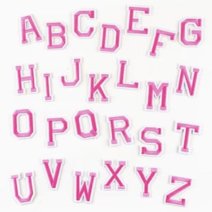 May include: A collection of twenty-six individual iron-on alphabet patches, each featuring a bold, block-style letter in a vibrant pink colour with a clean white border. The set includes every letter from A to Z, arranged in a grid-like layout.