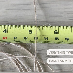 May include: A close-up of a thin, natural twine string measured against a yellow tape measure. The twine is approximately 1 to 1.5 millimeters thick. The text "VERY THIN TWINE, 1MM-1.5MM THICK" is visible below the twine.