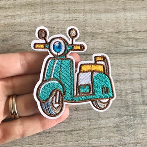 May include: A teal blue and white embroidered iron-on patch of a vintage scooter with brown details.