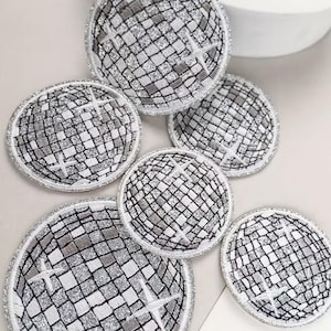 Könnte beinhalten: Eine Sammlung runder Untersetzer mit einem Discokugel-Design. Die Untersetzer haben ein silbernes Glitzermuster mit einem Gitter aus schwarzen Linien und einem silbernen Rand. Das Design beinhaltet einen weißen sternförmigen Akzent.