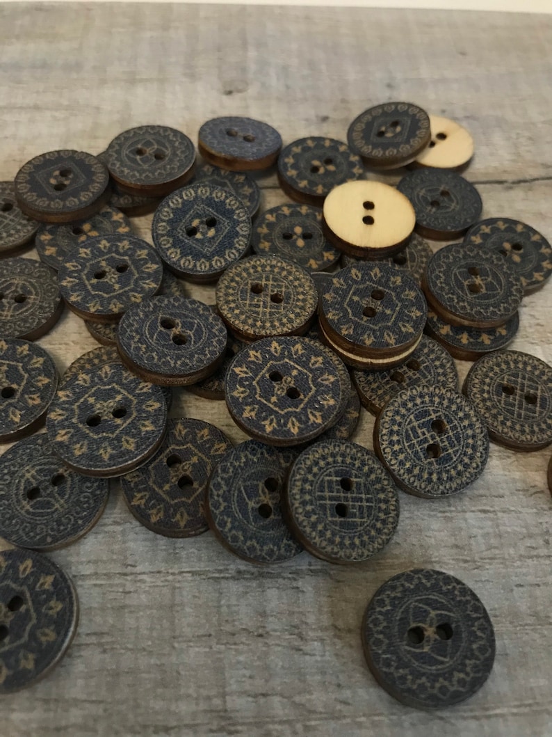 May include: A pile of wooden buttons with a dark blue and gold patterned design. The buttons are round and have two holes.