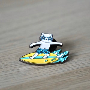 Puede incluir: Un gato blanco con gafas de sol y bañador azul y blanco está haciendo surf en una tabla de surf amarilla con olas azules.