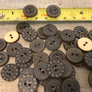 May include: A collection of wooden buttons with a black and gold geometric design. The buttons are scattered on a wooden surface.