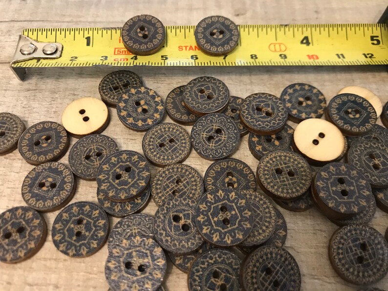 May include: A collection of wooden buttons with a black and gold geometric design. The buttons are scattered on a wooden surface.