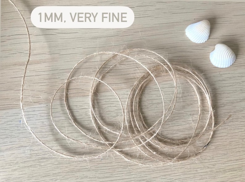 May include: A close-up of a natural fiber twine, 1 mm thick, labeled "1MM, VERY FINE". The twine is coiled on a light wood surface. Two white seashells are in the background.