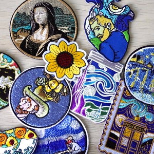 Pode incluir: Uma coleção de patches bordados para passar a ferro que representam pinturas famosas. Os patches incluem um girassol, um frasco com tinta azul e branca em espiral, uma onda, uma baleia, uma cena de noite estrelada e um retrato de uma mulher.