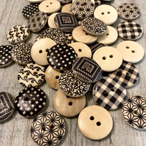 Könnte beinhalten: Eine Sammlung von Holzknöpfen mit verschiedenen schwarz-weißen Mustern, darunter geometrische Designs, Gingham und Wirbel. Die Knöpfe sind auf einer Holzoberfläche zu einem Stapel angeordnet.
