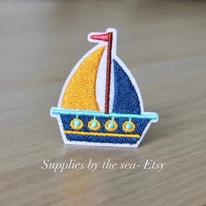 May include: A blue and yellow embroidered sailboat patch with a red flag. The sailboat has a white sail and a blue hull with yellow accents. The patch is perfect for adding a nautical touch to any project.