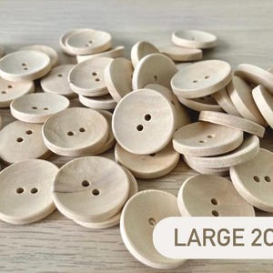 May include: A collection of large, natural wood buttons with two holes each. The buttons are round and have a light, neutral color. The text "LARGE 2cm" is visible in a tan rectangle.