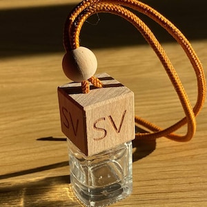 Può includere: Una piccola bottiglia di vetro trasparente con un tappo di legno. Il tappo ha le lettere "SV" incise. La bottiglia è attaccata a un lungo cordoncino arancione con un perno di legno.