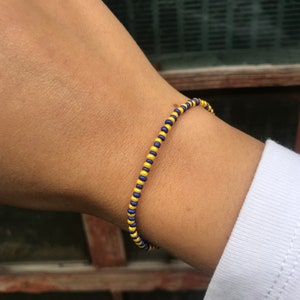May include: A yellow and blue beaded bracelet on a person's wrist.