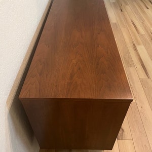 May include: A dark brown wooden dresser with a smooth, polished finish. The dresser has a rectangular shape and is sitting on a light wood floor.
