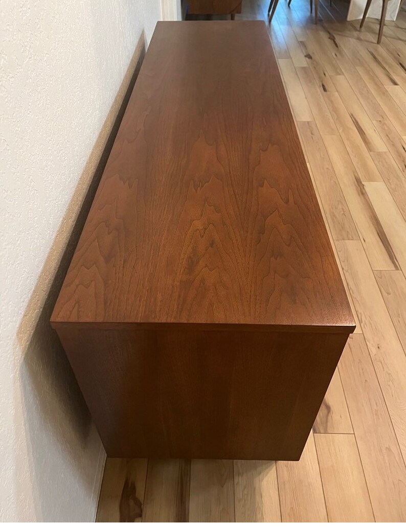 May include: A dark brown wooden dresser with a smooth, polished finish. The dresser has a rectangular shape and is sitting on a light wood floor.