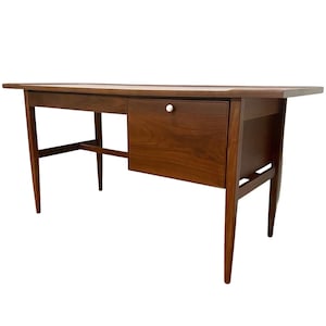 May include: A mid-century modern walnut desk with a single drawer and tapered legs. The desk has a simple design with a clean, minimalist aesthetic.