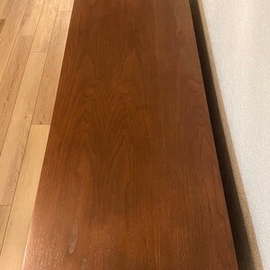 May include: A solid wood entertainment center with a rich brown finish. The top of the unit is flat and smooth, with a slight sheen. The unit has a simple, modern design.