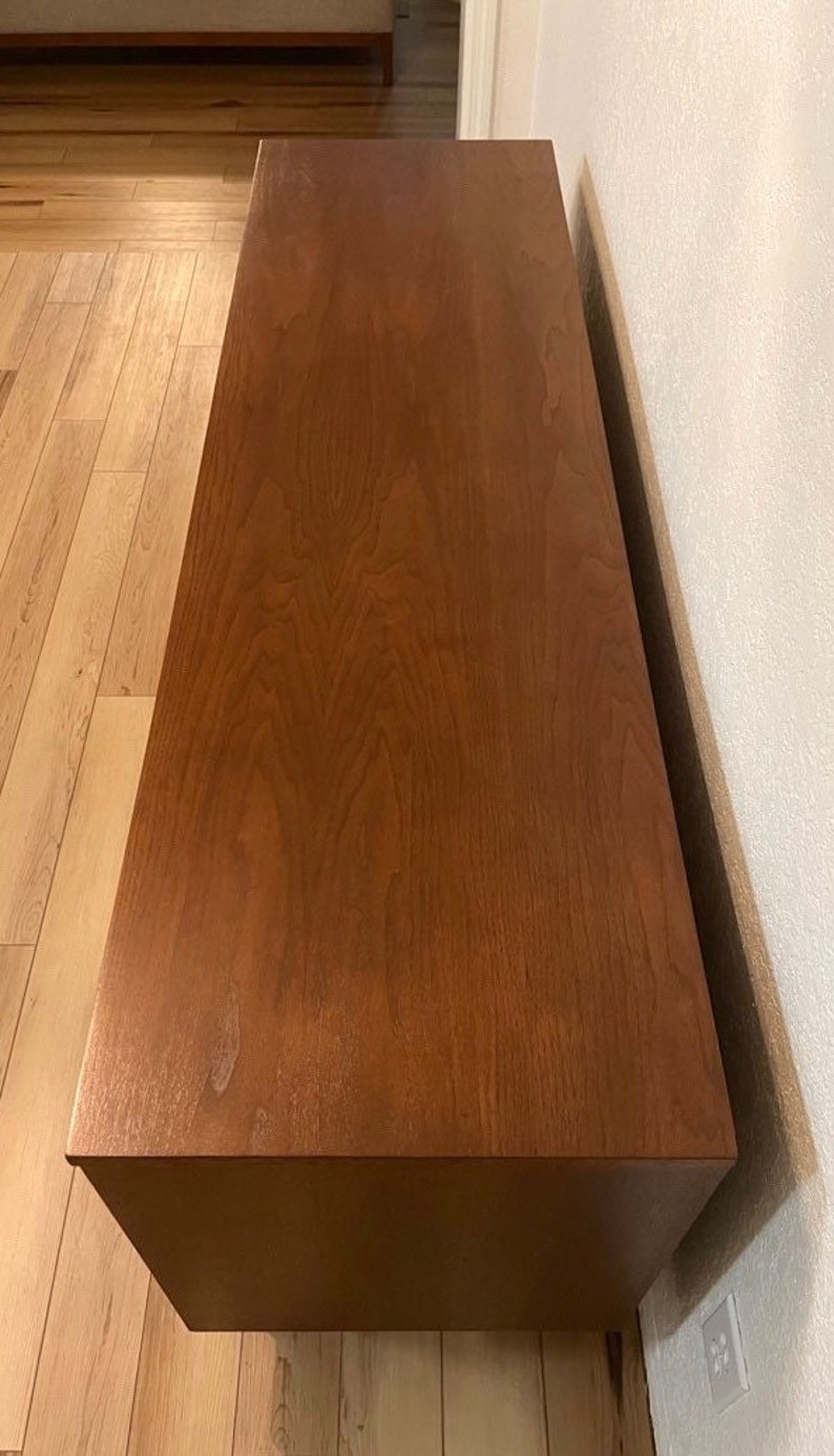 May include: A solid wood entertainment center with a rich brown finish. The top of the unit is flat and smooth, with a slight sheen. The unit has a simple, modern design.