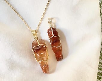 Pingente artesanal de cristal de calcita vermelha, com detalhes em fio de ouro e prata.