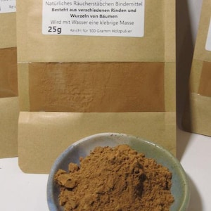 Könnte beinhalten: Ein brauner Papierbeutel mit einem weißen Etikett, auf dem "Natürliches Stäbchenpulver" steht. Das Etikett enthält auch Informationen über das Produkt, wie z. B. die Zutaten und die Anwendung. Der Beutel liegt auf einer weißen Oberfläche, und davor steht eine kleine Schüssel mit braunem Pulver.