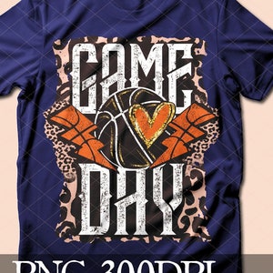 May include: A navy blue t-shirt with a distressed graphic design featuring a basketball with a heart and the text "GAME DAY" in white and orange. The background is a leopard print pattern.