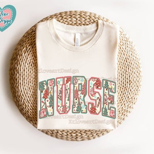 May include: A white t-shirt with the word "NURSE" printed in large, colourful letters. The letters are decorated with a floral pattern in shades of red, green, and blue.