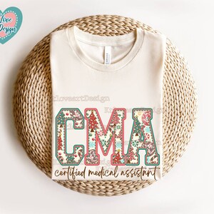 May include: A white t-shirt featuring a Christmas-themed design that reads "CMA certified medical assistant". The letters are decorated with a patchwork pattern of Christmas trees, baubles, and candy canes.