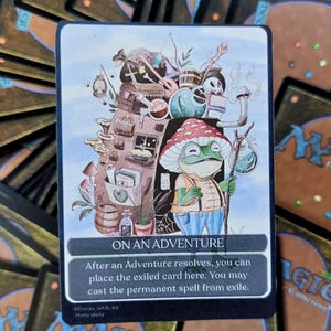 May include: A Magic: The Gathering card with a fantasy illustration of a frog in a mushroom hat, holding a staff. The card reads "ON AN ADVENTURE" with game instructions. Other Magic cards are visible in the background.
