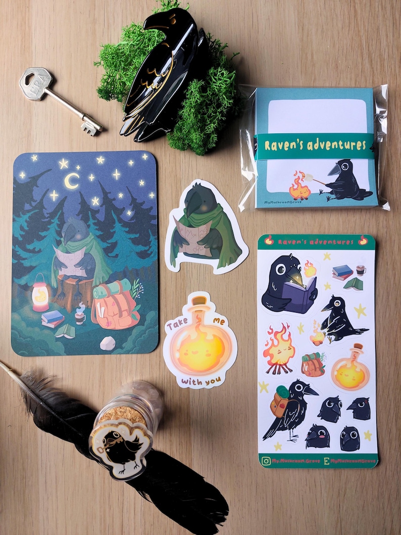 K&ouml;nnte beinhalten: Ein Set aus Schreibwaren mit Raben-Illustrationen, bestehend aus einem Notizblock mit der Aufschrift Raven's adventures, einer Postkarte, zwei Aufklebern, einem Stickerbogen, einer schwarzen Rabenfigur, einem Metallschl&uuml;ssel und einer schwarzen Feder.
