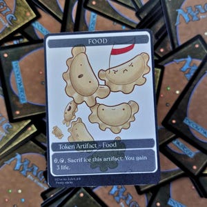 May include: A Magic: The Gathering card depicting cartoon pierogi with faces and a small flag. The card is labelled "Token Artifact - Food" and includes game text. Other Magic cards are in the background.