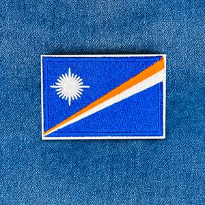 Puede incluir: Parche bordado con la bandera de las Islas Marshall. El parche rectangular tiene un fondo azul con una estrella blanca en la esquina superior izquierda. Una franja diagonal naranja y blanca atraviesa la bandera.