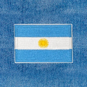 May include: Embroidered patch featuring the flag of Argentina. The design includes a light blue background with a white horizontal stripe in the center. A yellow sun is in the center of the white stripe. The patch is rectangular with a white border.