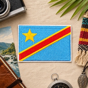 May include: Embroidered patch featuring the flag of the Democratic Republic of the Congo. The patch has a light blue background with a yellow star in the upper left corner and a red and yellow diagonal stripe. The patch is rectangular with a white border.