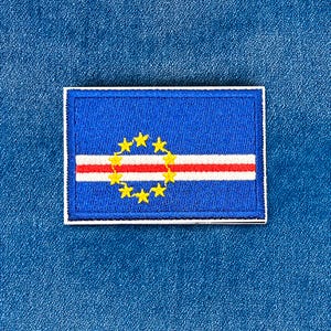 May include: A rectangular patch depicting the flag of Cape Verde. The patch has a blue background with a white border. A red and white stripe runs horizontally across the centre, with a ring of ten yellow stars above it.