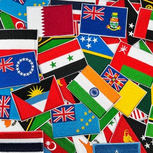 May include: A collection of rectangular embroidered patches featuring various national flags, including those of Qatar, Syria, India, and Tuvalu, arranged in a dense, overlapping pile with vibrant colors and detailed stitching visible.