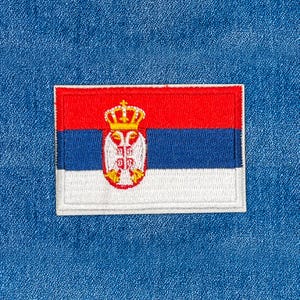 May include: Embroidered patch featuring the flag of Serbia. The rectangular patch has a red top stripe, a blue middle stripe, and a white bottom stripe. The Serbian coat of arms is in the center. The patch is on a blue denim background.