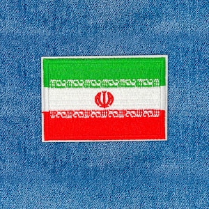 Könnte beinhalten: Gestickter Aufnäher mit der iranischen Flagge. Der rechteckige Aufnäher hat horizontale Streifen in Grün, Weiß und Rot. In der Mitte des weißen Streifens befindet sich ein rotes Emblem. Der Aufnäher ist vor einem blauen Jeans-Hintergrund angebracht.