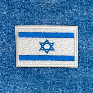 Könnte beinhalten: Gestickter Aufnäher mit der Flagge Israels. Der rechteckige Aufnäher hat einen weißen Hintergrund mit zwei horizontalen blauen Streifen und einem blauen Davidstern in der Mitte. Der Aufnäher ist von einer weißen Kontur umrandet und vor blauem Stoffhintergrund platziert.