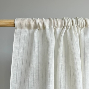 May include: White sheer curtain panel with thin gray stripes. The curtain is gathered at the top and hangs from a wooden rod.