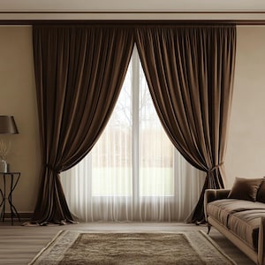 May include: A pair of brown velvet curtains hang in front of a window with sheer white curtains. The curtains are pulled back to reveal a view of trees and a house in the distance.