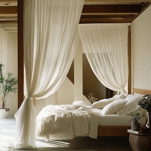 May include: A bedroom featuring a wooden bed frame and a canopy of cream-coloured, sheer curtains. The bed is dressed with white bedding and pillows. A small side table holds a vase of flowers.