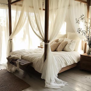 Pode incluir: Uma cama de dossel branca com um edredom e almofadas de linho branco. A cama é feita de madeira e tem uma cabeceira e um pé de cama de madeira. O dossel é feito de tecido branco transparente e pendura do teto. Há um pequeno banquinho de madeira no pé da cama.