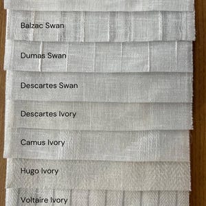 K&ouml;nnte beinhalten: Nahaufnahme von acht Stoffmustern in verschiedenen Wei&szlig;- und Elfenbeint&ouml;nen. Die Muster sind mit Namen wie "Balzac Swan", "Dumas Swan", "Descartes Ivory" und "Proust Sand" beschriftet.