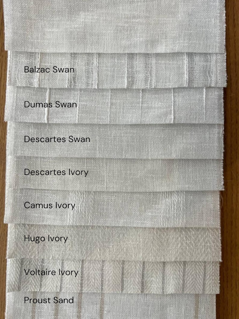 K&ouml;nnte beinhalten: Nahaufnahme von acht Stoffmustern in verschiedenen Wei&szlig;- und Elfenbeint&ouml;nen. Die Muster sind mit Namen wie "Balzac Swan", "Dumas Swan", "Descartes Ivory" und "Proust Sand" beschriftet.