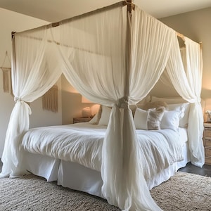 May include: A white canopy bed with a white bedspread and white pillows. The bed has a wooden frame and is draped with a sheer white fabric.
