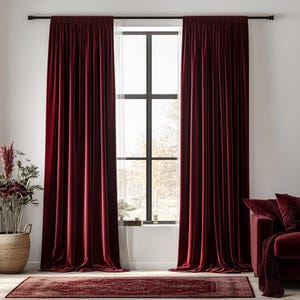 May include: Deep burgundy velvet curtains are draped on a black curtain rod, beside a window. A matching rug and sofa with cushions create a warm, inviting living space. A woven basket with plants is on the left.
