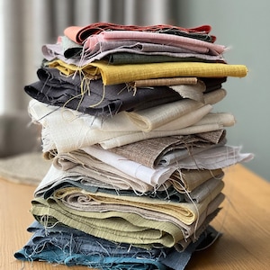 Op de afbeelding: Een stapel stofresten in verschillende kleuren en texturen, waaronder beige, bruin, grijs, blauw, groen en geel.