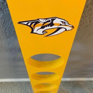 May include: Yellow wooden display stand with three circular holes, featuring the Nashville Predators logo. The top edge is painted navy blue. The stand is designed to hold items and is suitable for home decor.